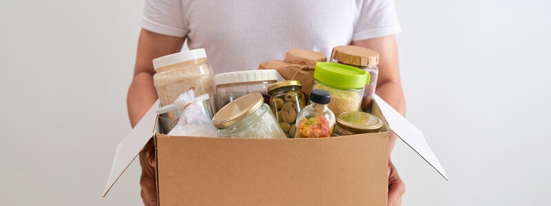 young man holding a cardboard box full of food supplies